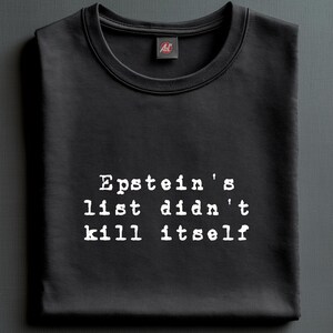 Może przedstawiać: Czarna bluza z okrągłym dekoltem z napisem "Epstein's list didn't kill itself" czcionką z maszyny do pisania. Mała metka jest widoczna w pobliżu kołnierza. Bluza jest starannie złożona.