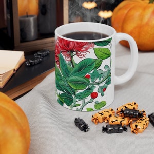 May include: White ceramic mug with a floral design featuring red flowers, green leaves, and red berries. The mug is filled with dark coffee and has a white handle.