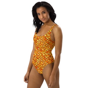 Puede incluir: Un traje de baño de una pieza con un patrón de escamas de pez doradas y naranjas.