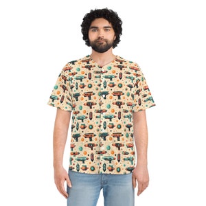 May include: A short-sleeved button-up shirt with a beige background and a repeating pattern of colorful ray guns, planets, and stars. The shirt has a classic collar and is worn with blue jeans.