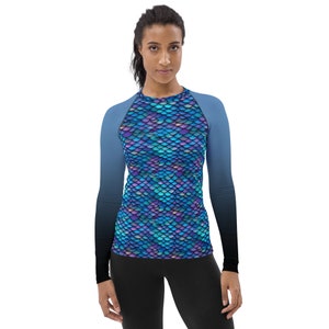 May include: A long-sleeved shirt with a mermaid scale pattern in shades of blue, purple, and green. The shirt has a black and blue ombre effect on the sleeves.