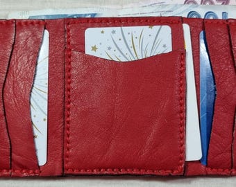 May include: Open red leather wallet with multiple card slots and a snap closure. The wallet is filled with cards and folded bills. The stitching is visible around the edges.