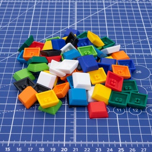 Könnte beinhalten: Ein Haufen bunter Plastik-Tastenkappen in verschiedenen Farben, darunter Rot, Blau, Grün, Gelb und Weiß. Die Tastenkappen sind in einem zufälligen Muster auf einer blauen, gerasterten Oberfläche angeordnet.