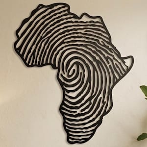 Op de afbeelding: Zwart metalen wandkunstwerk in de vorm van het Afrikaanse continent, met een vingerafdrukontwerp. De kunst wordt getoond op een beige muur, samen met ingelijste foto's en decoratieve maskers. De kamer is ingericht met een bank, kussens en een houten salontafel.