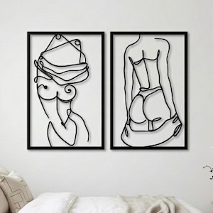 Puede incluir: Dos obras de arte murales enmarcadas en negro. La pieza de la izquierda es un dibujo lineal de la parte superior del cuerpo y la cabeza de una persona. La pieza de la derecha es un dibujo lineal de la espalda y la parte inferior del cuerpo de una persona. Ambas piezas est&aacute;n montadas en una pared blanca.