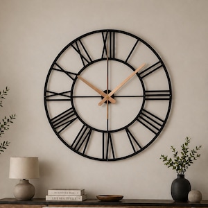 May include: A large, round black metal wall clock with Roman numerals and light brown clock hands. The clock is mounted on a light-coloured wall above a sofa. The room is decorated in neutral tones with a modern aesthetic.