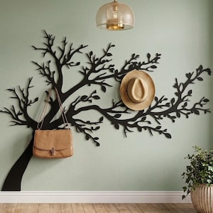 Puede incluir: Arte mural de árbol de metal negro con un bolso de mano marrón y un sombrero de paja colgados de las ramas. La pared está pintada de color verde claro y el suelo es de madera.