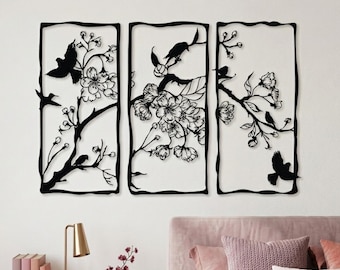 May include: A three-piece black metal wall art set featuring intricate silhouettes of flowering cherry blossom branches and birds. Each rectangular panel displays a unique arrangement of blossoms and birds, creating a cohesive nature-inspired design.