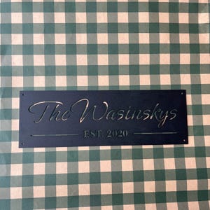 a black rectangular sign with the text "The Wainskys EST. 2020" on it, placed on a green and white checkered background.