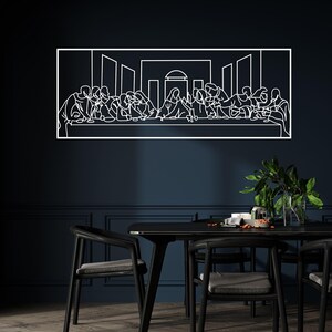 May include: A white line art depiction of The Last Supper, framed in a rectangular shape. The artwork is mounted on a dark blue wall above a black dining table and chairs. A vase of green plants is on the table.
