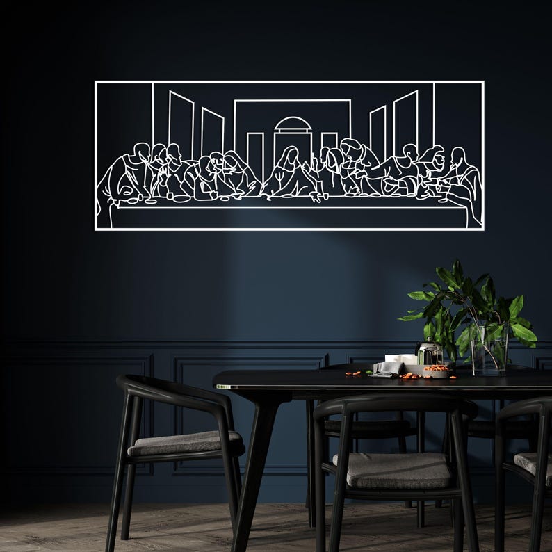 May include: A white line art depiction of The Last Supper, framed in a rectangular shape. The artwork is mounted on a dark blue wall above a black dining table and chairs. A vase of green plants is on the table.