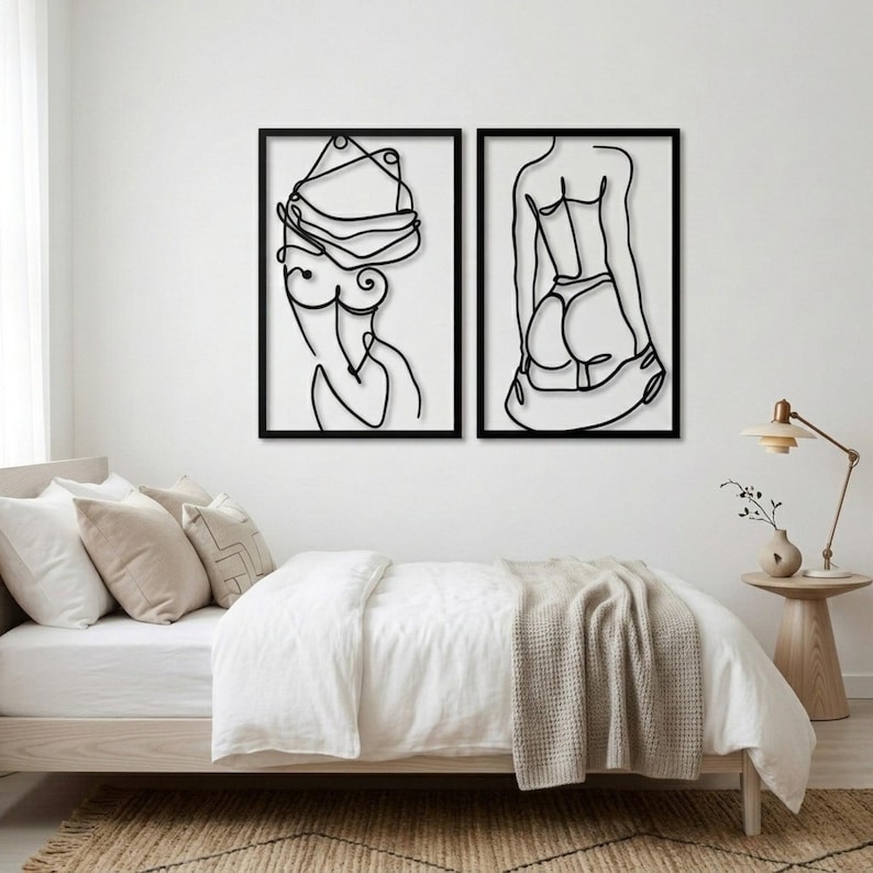 Puede incluir: Dos obras de arte murales enmarcadas en negro. La pieza de la izquierda es un dibujo lineal de la parte superior del cuerpo y la cabeza de una persona. La pieza de la derecha es un dibujo lineal de la espalda y la parte inferior del cuerpo de una persona. Ambas piezas est&aacute;n montadas en una pared blanca.