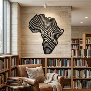 Op de afbeelding: Een zwart-wit kunstwerk in de vorm van het Afrikaanse continent, met een vingerafdrukontwerp. Het kunstwerk is gemonteerd op een bakstenen muur in een bibliotheek, met boekenplanken en een leren fauteuil.