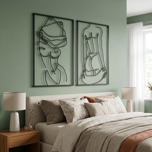 Puede incluir: Dos piezas de arte mural de metal negro que representan figuras femeninas en un estilo minimalista. La obra de arte est&aacute; enmarcada y montada en una pared verde claro sobre una cama con ropa de cama y almohadas de tonos neutros. Dos l&aacute;mparas a juego est&aacute;n en las mesitas de noche.