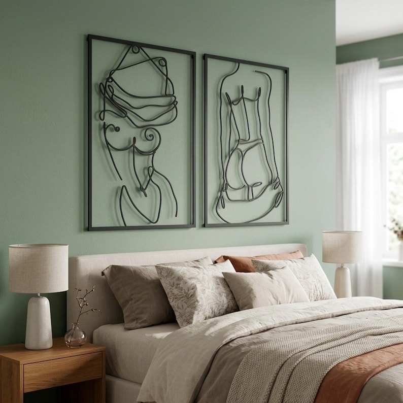 Puede incluir: Dos piezas de arte mural de metal negro que representan figuras femeninas en un estilo minimalista. La obra de arte est&aacute; enmarcada y montada en una pared verde claro sobre una cama con ropa de cama y almohadas de tonos neutros. Dos l&aacute;mparas a juego est&aacute;n en las mesitas de noche.