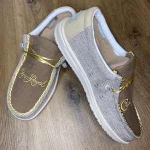 May include: A pair of brown and beige slip-on shoes with a gold embroidered logo that says "Crown Royal".