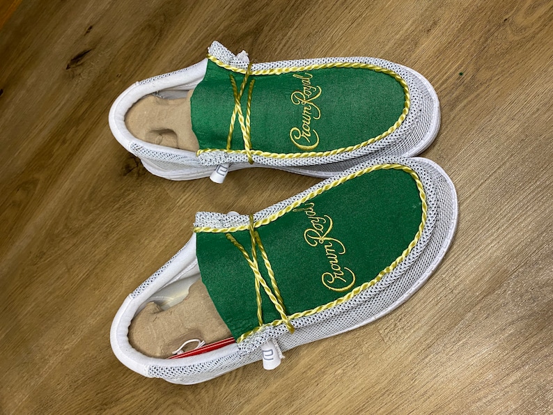 May include: A pair of white slip-on shoes with green fabric uppers and gold embroidery that reads "Crown Royal".