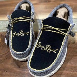 May include: A pair of gray and black slip-on shoes with a gold embroidered "Crown Royal" logo on each shoe.