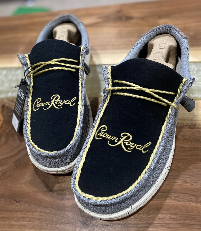 May include: A pair of gray and black slip-on shoes with a gold embroidered "Crown Royal" logo on each shoe.