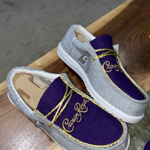 May include: A pair of gray slip-on shoes with a purple and gold "Crown Royal" logo embroidered on the top.