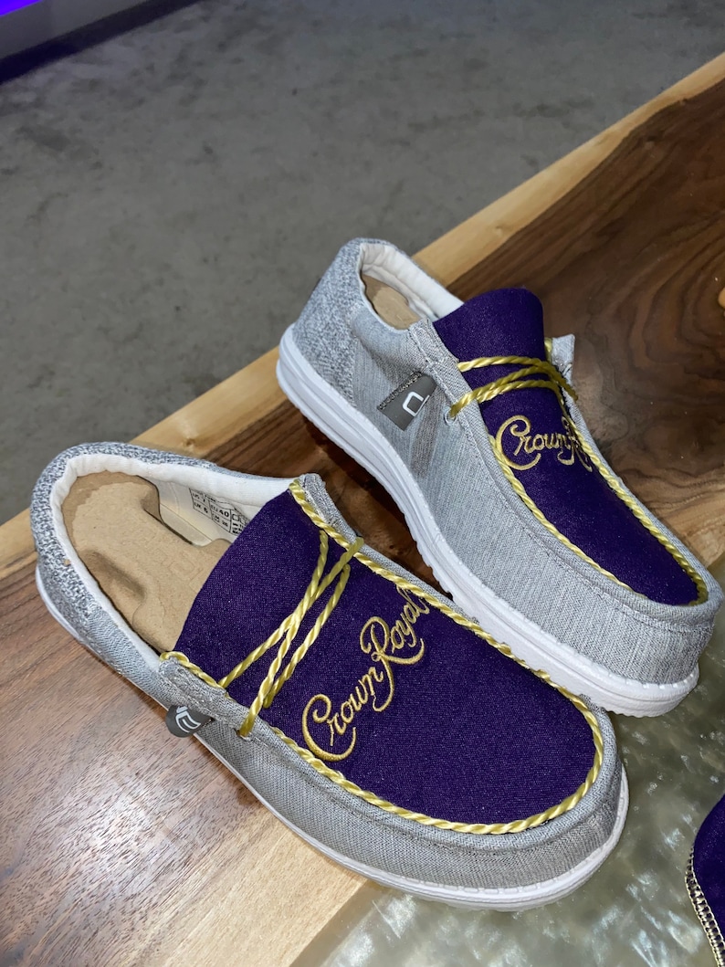 May include: A pair of gray slip-on shoes with a purple and gold "Crown Royal" logo embroidered on the top.