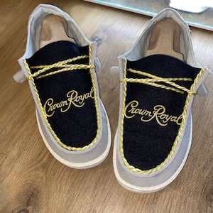 May include: A pair of gray and black slip-on shoes with gold rope trim and "Crown Royal" embroidered on the front.