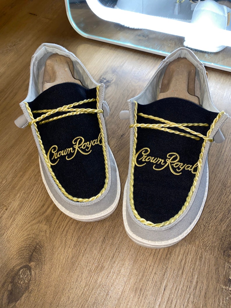 May include: A pair of gray and black slip-on shoes with gold rope trim and "Crown Royal" embroidered on the front.