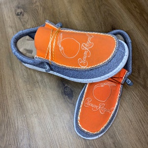 May include: A pair of orange and gray slip-on shoes with a peach design and the text "Crown Royal" embroidered on the top.