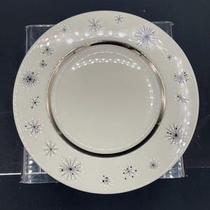 Op de afbeelding: Een wit keramiek dinerbord met een zilveren rand en een zwart-wit stervormig ontwerp.