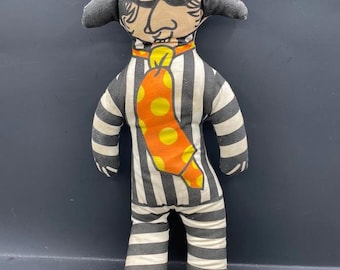May include: A handmade fabric doll in a prisoner costume. The doll has a painted face with a black mask, a striped outfit, and yellow boots. The tie is orange with yellow polka dots. The hat is yellow and gray.