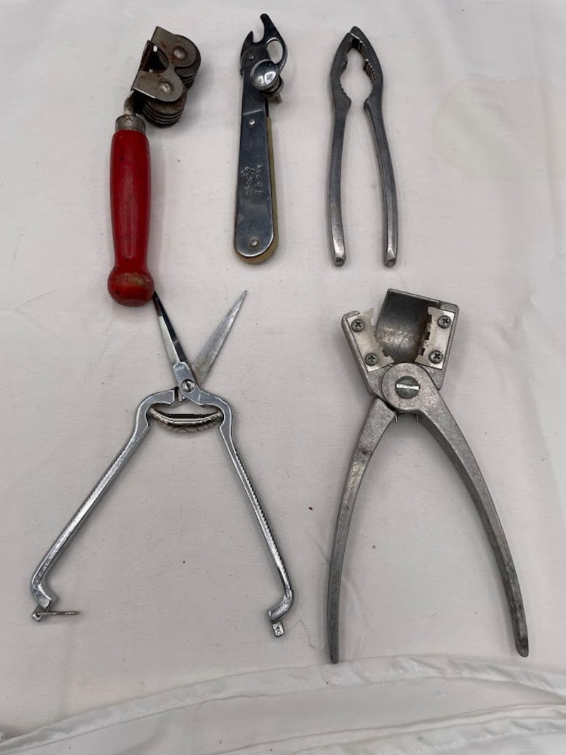 May include: Five different kitchen tools, including a can opener, nutcracker, and a pair of scissors. The tools are all made of metal and have a silver finish.