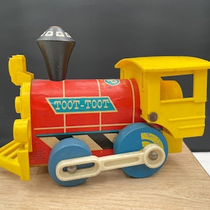 May include: A vintage red, yellow, and blue Toot-Toot train engine toy with a black chimney and a pull string. The engine has a yellow cab with a window and a blue wheel with a white rim.
