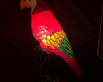Lampada d'accento a forma di pappagallo in vetro rosa, giallo e verde con testa in plastica e base in metallo.