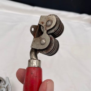 May include: A vintage knife sharpener with a red wooden handle and a metal sharpening mechanism with multiple wheels.