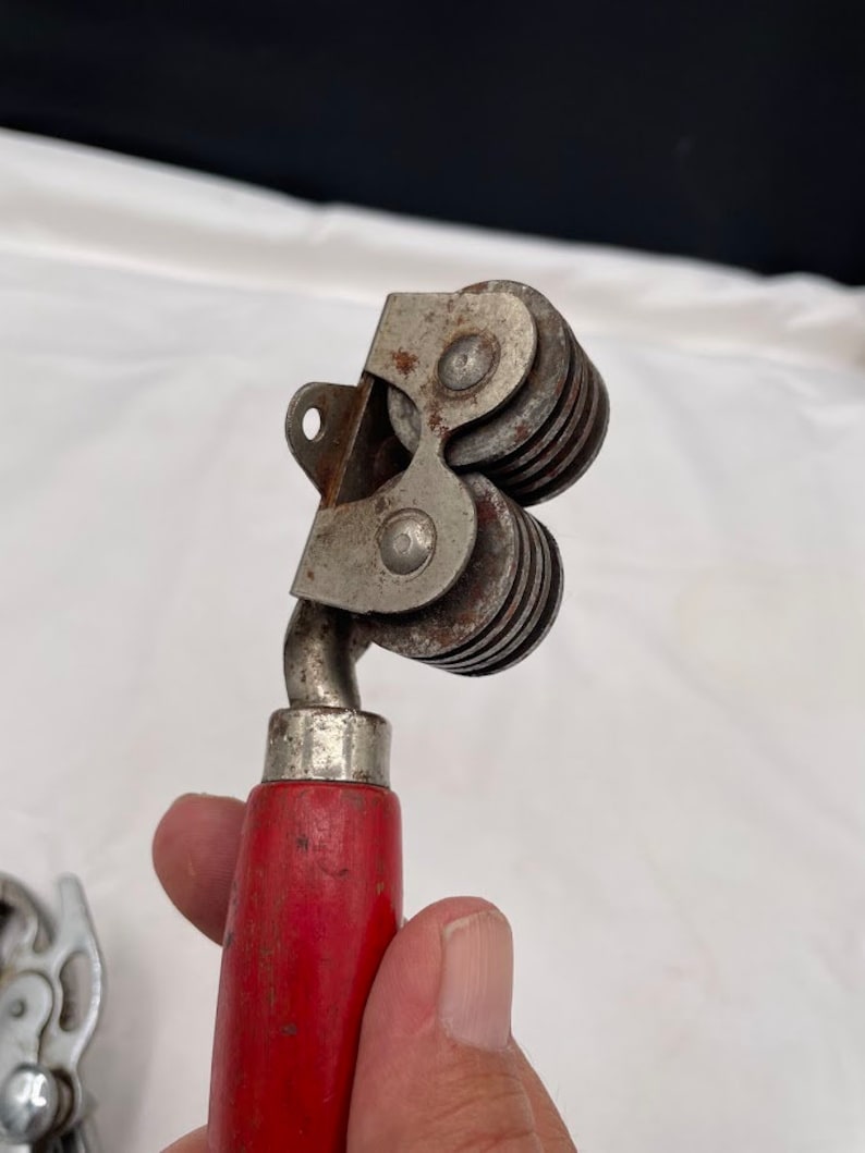 May include: A vintage knife sharpener with a red wooden handle and a metal sharpening mechanism with multiple wheels.