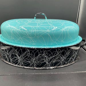 May include: A vintage turquoise and black enamelware casserole dish with a lid. The turquoise lid features a white scribble pattern and a handle. The black base has a matching white scribble design and two handles.