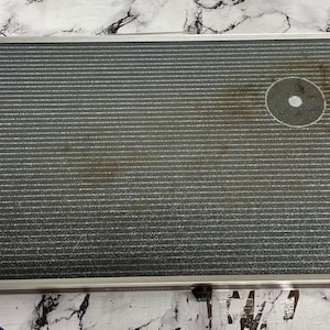 May include: A rectangular serving tray featuring a dark gray surface with fine horizontal white lines and a circular center detail. The tray is framed in silver-toned metal and includes two long, smooth wooden handles attached to the sides.