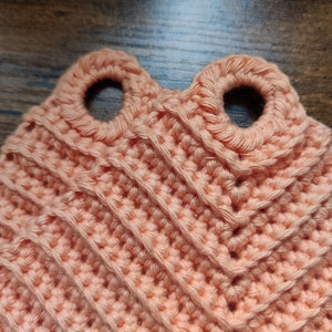 Könnte beinhalten: Nahaufnahme eines peachfarbenen gehäkelten Topflappen mit zwei Schlaufen zum Aufhängen. Die Schlaufen sind mit einer festen Masche gehäkelt.