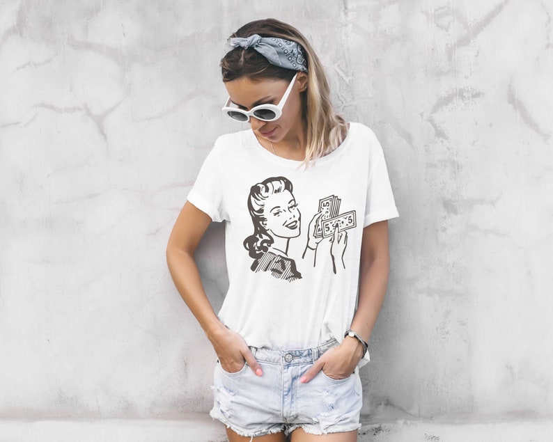 May include: White t-shirt with a vintage illustration of a woman holding a stack of money. The woman is smiling and looking at the money. The text on the money is "$100".
