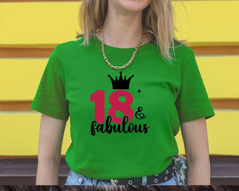 以下が含まれることがあります： 緑色のTシャツに、ピンクの数字18と黒い文字で「& fabulous」と書かれている。数字18の上に黒い王冠がある。