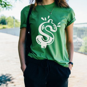 May include: A green t-shirt with a white dollar sign graphic. The dollar sign is stylized with a cartoonish design.