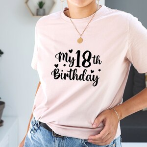 以下が含まれることがあります： ハートと星がついた黒い文字で「My 18th Birthday」と書かれたピンクのTシャツです。