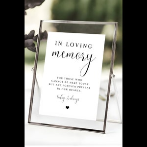 May include: A white sign with black text in a clear acrylic frame. The sign reads "In loving memory" and "For those who cannot be here today but are forever present in our hearts. Today & always".