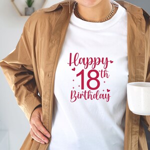 以下が含まれることがあります： 赤いハートと星がついた赤い文字で「Happy 18th Birthday」と書かれた白いTシャツです。