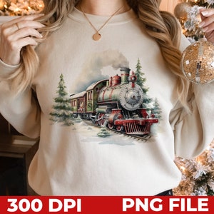 May include: A white sweatshirt with a vintage-style illustration of a green and red steam train traveling through a snowy winter forest. The train has a large smokestack and is decorated with red and white accents.