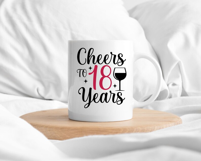 以下が含まれることがあります： 白いセラミック製のマグカップに、黒い文字で「Cheers to 18 Years」と書いてあり、18は赤色で、ワイングラスの黒いシルエットが描かれています。