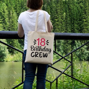 以下が含まれることがあります： ピンクの数字18で「18 Birthday Crew」と書かれた黒いテキストの入ったベージュのトートバッグです。