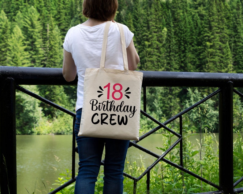 以下が含まれることがあります： ピンクの数字18で「18 Birthday Crew」と書かれた黒いテキストの入ったベージュのトートバッグです。