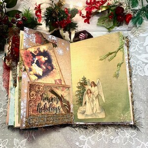 May include: Open journal with decorative pages, featuring a "Happy Holidays" card and angel illustration. The journal is adorned with festive embellishments, including red berries and greenery, creating a holiday theme.