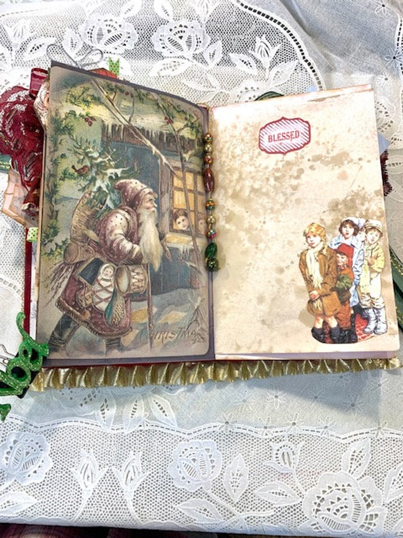 May include: Open journal with vintage Christmas illustrations. One page shows Santa Claus, the other has children and the word "Blessed" in a red label. The journal has a gold fringe and a beaded spine.
